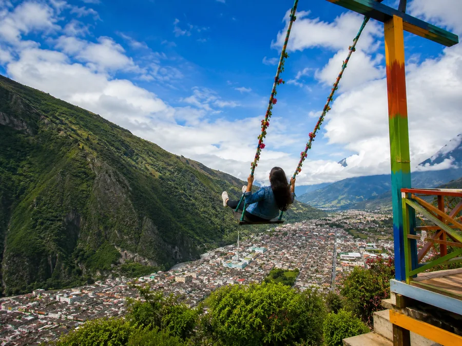 Person swinging with a view of the Andes mountains and city.